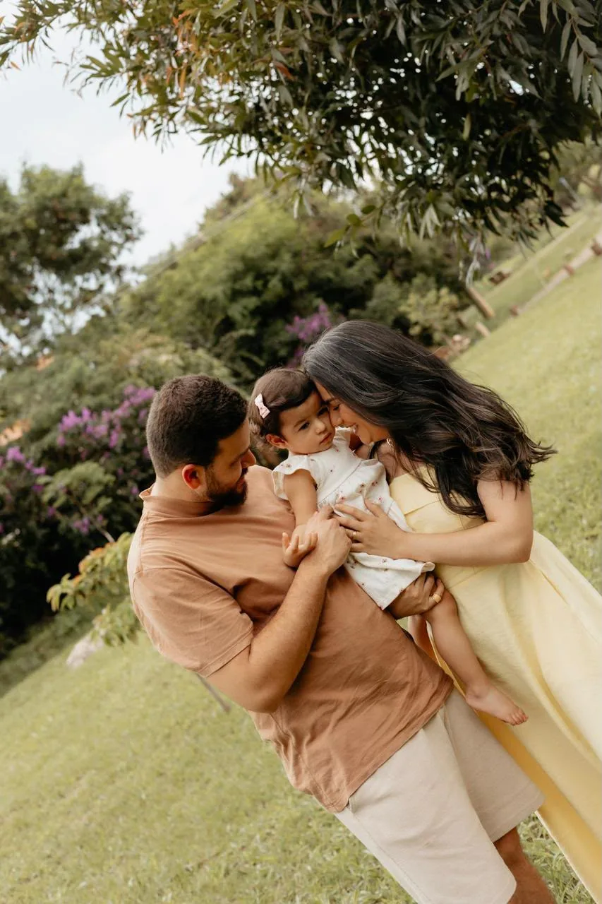 Pai, mãe e filha se abraçando num jardim florido