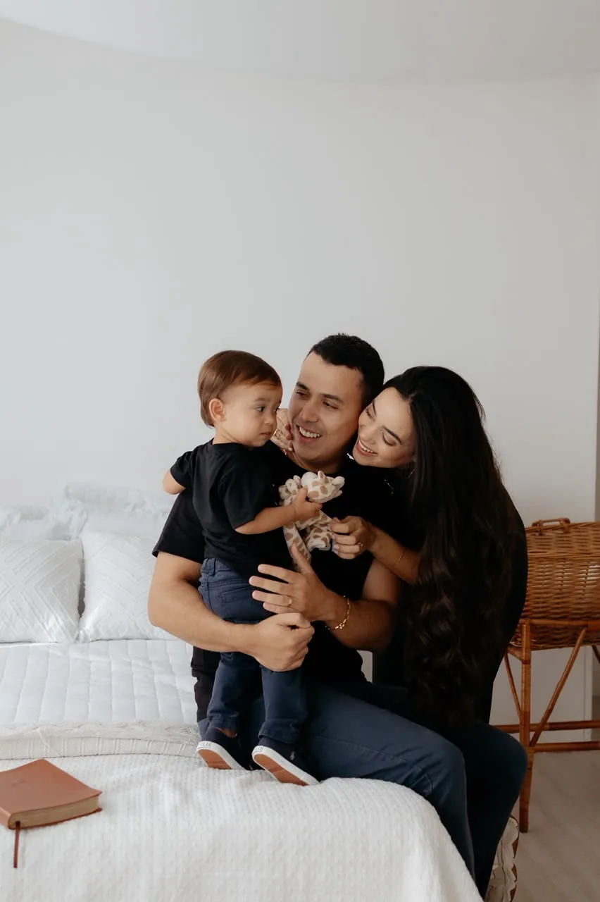 Família sorrindo na cama do estúdio durante o ensaio gestante