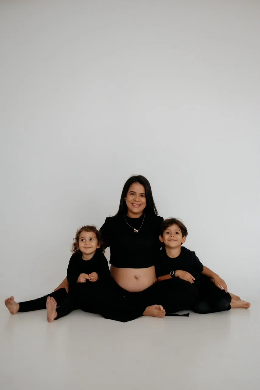 Gestante sentada no chão do estúdio entre os dois filhos