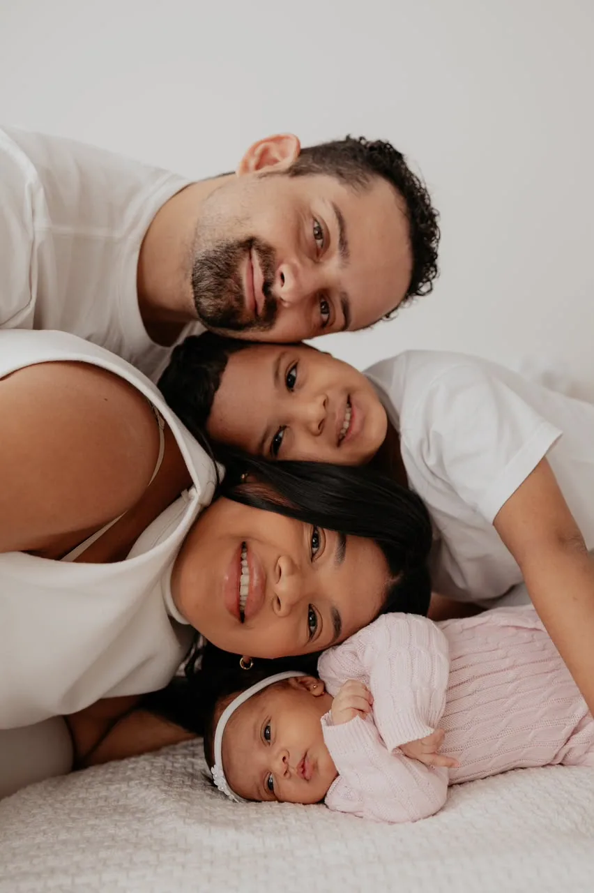 Família deitada na cama com os rostos colados e a bebê caçula na frente