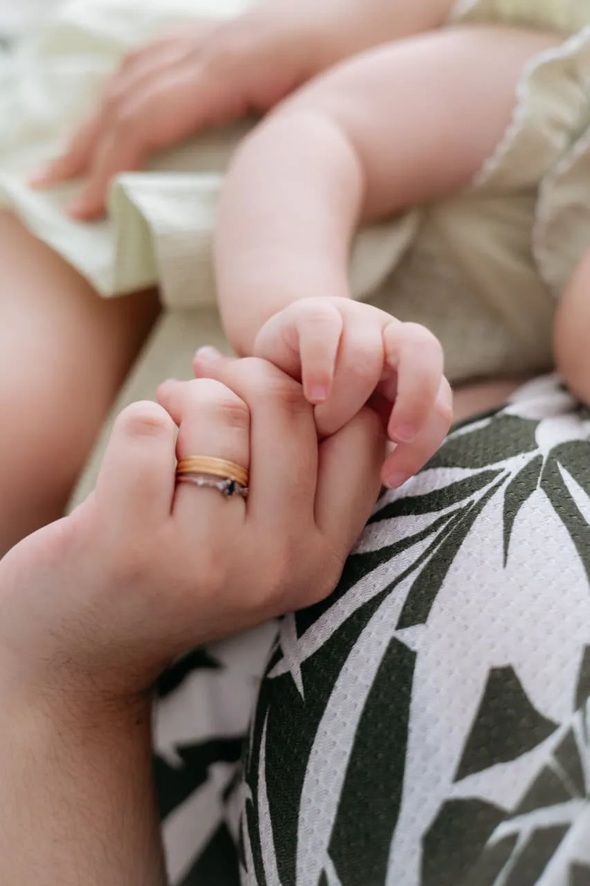 Mãozinha do bebê segurando o dedo da mãe, com a aliança
